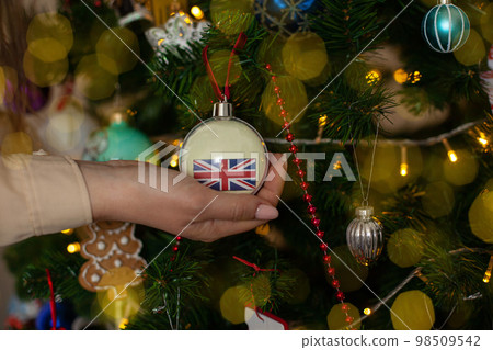 a girl holds a decoration on a Christmas tree with the flag of Great Britain a girl holds a decoration on a Christmas tree with the flag of Great Britain 98509542