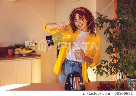Curly-haired girl pouring smoothie to the glass Curly-haired girl pouring smoothie to the glass 98509691
