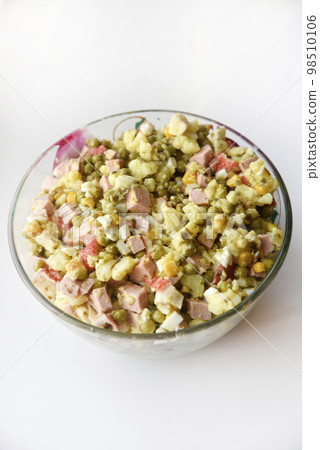 New Year's salad of meat vegetables and mayonnaise in a large plate. Delicious salad with corn and potatoes. New Year's salad of meat vegetables and mayonnaise in a large plate. Delicious salad with corn and potatoes. 98510106