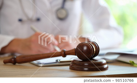 Wooden judge gavel on medical clinic desk and doctor doing paperwork in background. 98510766