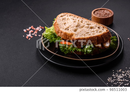 Fresh tasty sandwich with chicken, tomatoes and lettuce on a black plate 98511003