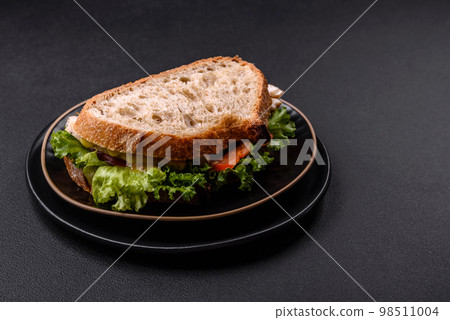 Fresh tasty sandwich with chicken, tomatoes and lettuce on a black plate Fresh tasty sandwich with chicken, tomatoes and lettuce on a black plate 98511004