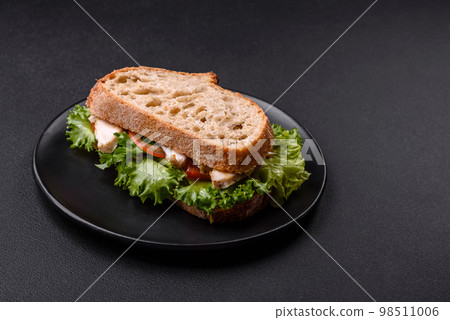 Fresh tasty sandwich with chicken, tomatoes and lettuce on a black plate 98511006