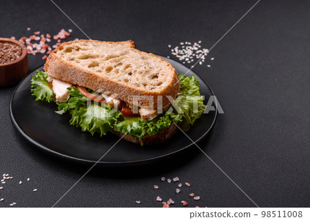 Fresh tasty sandwich with chicken, tomatoes and lettuce on a black plate Fresh tasty sandwich with chicken, tomatoes and lettuce on a black plate 98511008