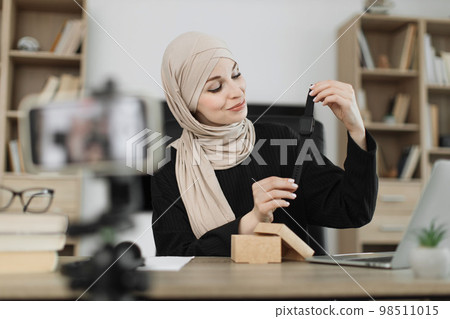 Muslim woman doing live stream while unpacking box with new smart watch. Muslim woman doing live stream while unpacking box with new smart watch. 98511015