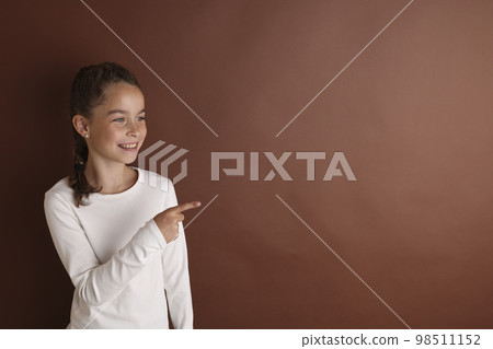 Little emotional teen girl in white 11, 12 years old on an isolated brown, chocolate background. Children's studio portrait. Place text, to copy space for inscription, advertising children's goods. 98511152