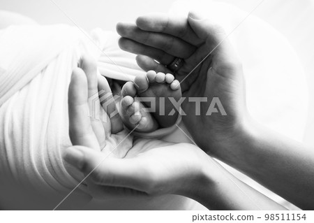 Little feet of a newborn in the hands of mom. The loving palm hand of a mother. Concept image of motherhood. Close-up, selective focus. Black and white professional photography. 98511154