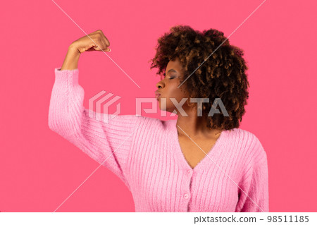 Happy young african american curly woman showing biceps on arm, kissing muscles Happy young african american curly woman showing biceps on arm, kissing muscles 98511185