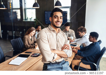 Successful person. Confident arab businessman leaning on desk in office, posing with folded arms and smiling at camera 98511197