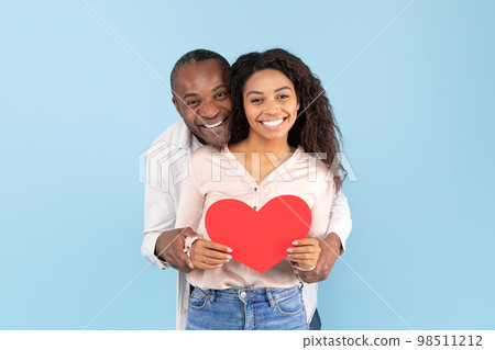 Loving african american couple celebrating their love, black middle aged man and young woman holding big red heart 98511212