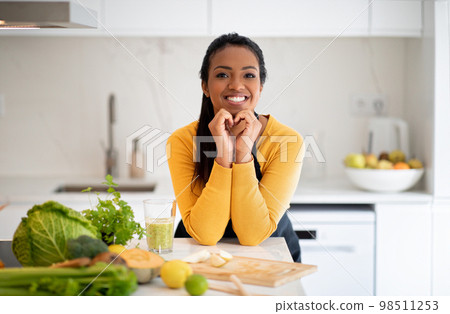 Happy young african american lady make heart sign with hands at table with organic vegetables, fresh smoothie 98511253