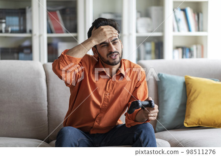 Sad arab guy playing video games at home, holding joystick 98511276