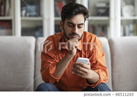 Thoughtful handsome middle eastern man using phone at home Thoughtful handsome middle eastern man using phone at home 98511283