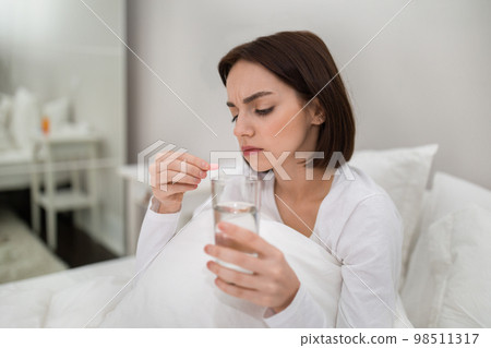 Young woman holding glass of water and pink capsule Young woman holding glass of water and pink capsule 98511317