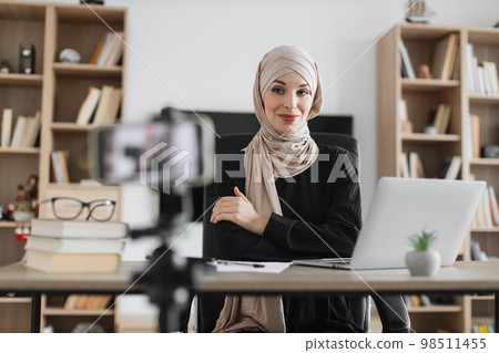 Beautiful muslim woman in hijab talking while looking at and recording video on modern smartphone. Beautiful muslim woman in hijab talking while looking at and recording video on modern smartphone. 98511455