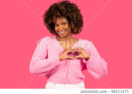 Happy pretty young african american curly woman with braces in casual outfit showing heart sign with hands Happy pretty young african american curly woman with braces in casual outfit showing heart sign with hands 98511471