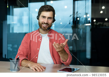 Webcam pov view, man in office with headset for video call smiling and looking into camera, businessman seller online communicates with customers, works remotely laptop at online meeting colleagues 98513035