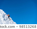 A climber in a red suit climbs an icy white mountain 98513268