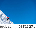 A climber in a red suit climbs an icy white mountain 98513271