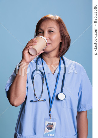 Senior asian nurse holding beverage cup drinking coffee before checkup visit appointment, health care service. Physician medical assistant working at patient disease expertise. Medicine concept 98513586