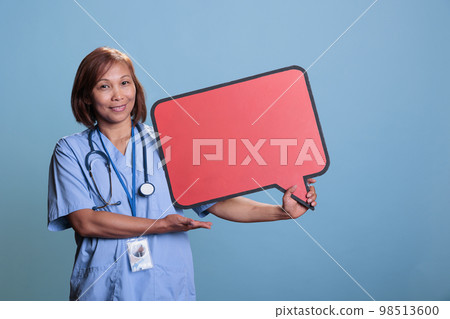 Elderly medical assistant holding cardboard speech bubble sign during checkup visit in studio with blue background. Asian nurse with stethoscope advertisement carton board. Medicine concept Elderly medical assistant holding cardboard speech bubble sign during checkup visit in studio with blue background. Asian nurse with stethoscope advertisement carton board. Medicine concept 98513600