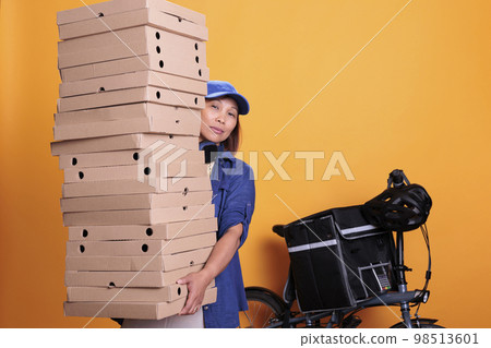 Large stack of pizza being carried by delivery woman in uniform for one of restaurant clients during lunk time. Elderly asian employee deliverying food order with bike, take away concept Large stack of pizza being carried by delivery woman in uniform for one of restaurant clients during lunk time. Elderly asian employee deliverying food order with bike, take away concept 98513601