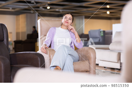 Girl checks high quality of armchair in furniture store 98515350