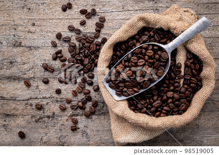 Background of dark roasted coffee beans with scoops setup on wooden background with copy space. 98519005