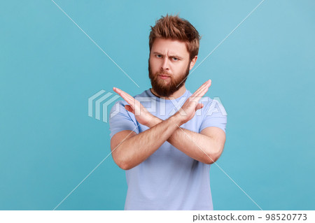 There is no way. Portrait of concerned disappointed handsome bearded man showing x sign with crossed hands, meaning stop, finish. Indoor studio shot isolated on blue background. 98520773