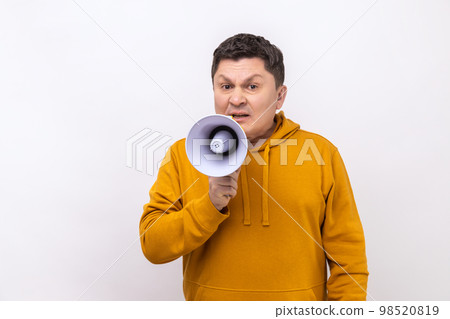 Optimistic middle aged man screaming in megaphone, announcing important information with positive, looking at camera, wearing urban style hoodie. Indoor studio shot isolated on white background. Optimistic middle aged man screaming in megaphone, announcing important information with positive, looking at camera, wearing urban style hoodie. Indoor studio shot isolated on white background. 98520819
