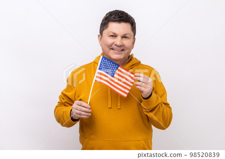 Portrait of smiling middle aged man holding USA national flag, celebrating national Independence Day - 4th july, wearing urban style hoodie. Indoor studio shot isolated on white background. 98520839