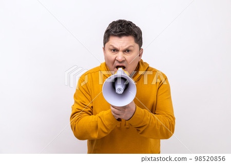 Portrait of dark haired middle aged handsome man screaming in megaphone, announcing important information, wearing urban style hoodie. Indoor studio shot isolated on white background. 98520856