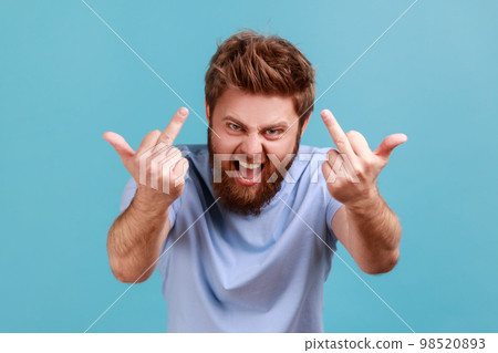 Portrait of furious aggressive handsome bearded man showing middle fingers, impolite rude gesture of disrespect, fuck off expression. Indoor studio shot isolated on blue background. 98520893