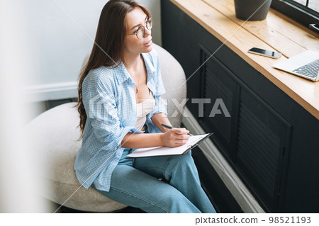 Young woman in bue shirt with notes in hands sitting on chair in room Young woman in bue shirt with notes in hands sitting on chair in room 98521193