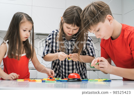 Portrait of group of focused friends standing at table, playing board game ring, buckling geometric shapes in chain. 98525423