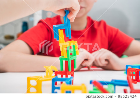 Cropped photo of preteen children playing board game stacking chairs, putting small chairs in stack for building tower. 98525424