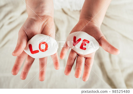 Hands of little girl hold two white smooth stones with syllables lo and ve painted red on white cloth background. Love Hands of little girl hold two white smooth stones with syllables lo and ve painted red on white cloth background. Love 98525480