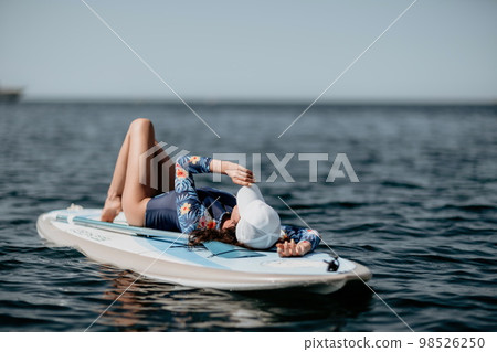 Woman sup yoga. Middle age sporty woman practising yoga pilates on paddle sup surfboard. Female stretching doing workout on sea water. Modern individual female hipster outdoor summer sport activity. 98526250