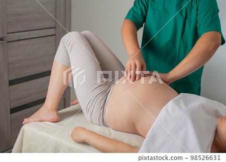 A chiropractic osteopathic doctor makes a massage to a pregnant girl in the 3rd trimester, background. Pregnant tummy A chiropractic osteopathic doctor makes a massage to a pregnant girl in the 3rd trimester, background. Pregnant tummy 98526631