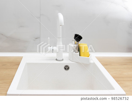 Beautiful kitchen interior of a white sink with a water faucet, sponge and brush for washing dishes and detergent against a white tile wall. Modern interior 98526732