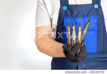 Car mechanic holds fuel car injectors in his hand. The concept of replacing and tuning the fuel system of a car at a car service. Copy space for text Car mechanic holds fuel car injectors in his hand. The concept of replacing and tuning the fuel system of a car at a car service. Copy space for text 98526740
