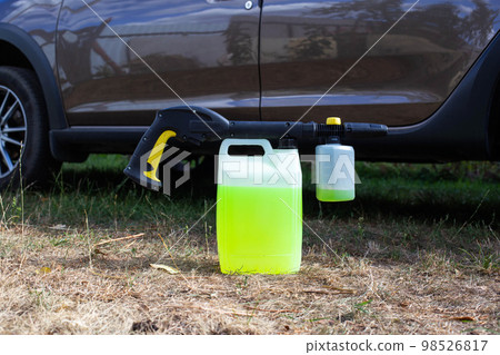 a canister with shampoo and a nozzle for a high-pressure washer a foam generator against the background of a car. Car wash and care. Copy space for text 98526817