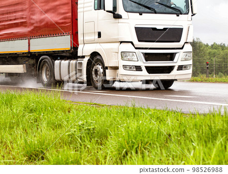 A truck with a semi-trailer transports cargo in rainy weather on a slippery road. Automobile cargo transportation. Copy space for text A truck with a semi-trailer transports cargo in rainy weather on a slippery road. Automobile cargo transportation. Copy space for text 98526988