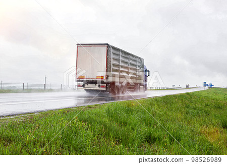 A truck with a semi-trailer transports cargo in rainy weather on a slippery road. Automobile cargo transportation. Copy space for text 98526989