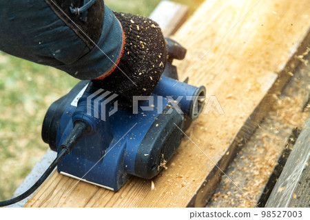 A man works with an electric tool with an electric planer, cleans old wood. Industry, close-up A man works with an electric tool with an electric planer, cleans old wood. Industry, close-up 98527003
