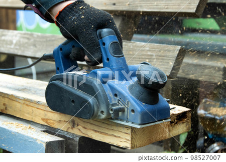 A man works with an electric tool with an electric planer, cleans old wood. Industry, close-up A man works with an electric tool with an electric planer, cleans old wood. Industry, close-up 98527007