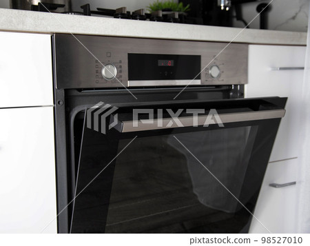 Black modern electric oven built into a white kitchen. Multifunction oven with grill Black modern electric oven built into a white kitchen. Multifunction oven with grill 98527010