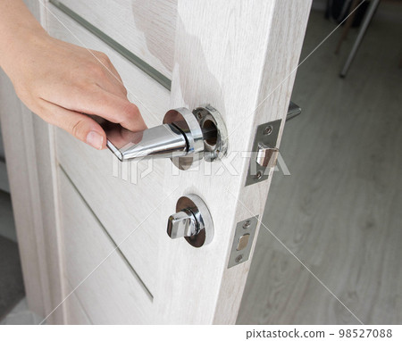 A man's hand opens an interior door with a broken doorknob. Poor quality door hardware, breakage, damage. A man's hand opens an interior door with a broken doorknob. Poor quality door hardware, breakage, damage. 98527088