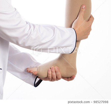 The phlebologist doctor selects the size of the patient's compression stockings. White background, close-up. The phlebologist doctor selects the size of the patient's compression stockings. White background, close-up. 98527098