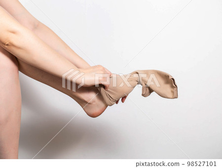 A woman puts on compression stockings for legs with varicose veins. Pain and swelling in the legs, phlebology. White background, close-up. Bloodstream 98527101